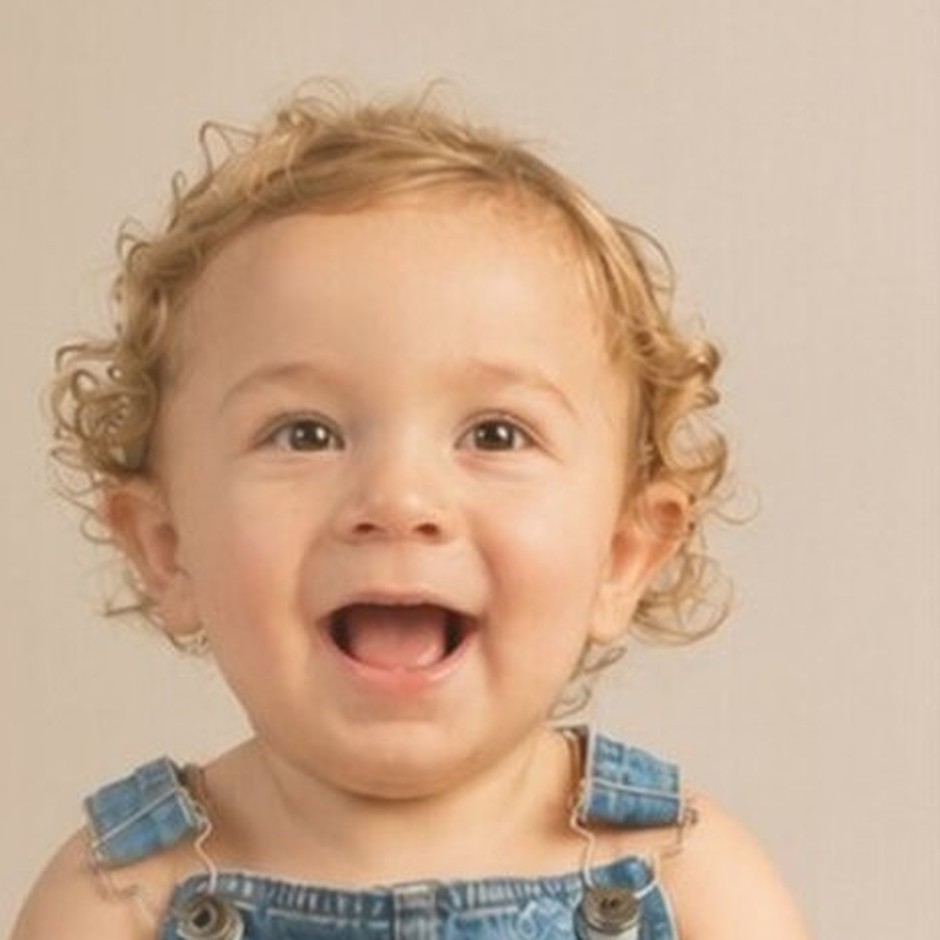Léo, um bebê de cabelos cacheados loiros, sorrindo